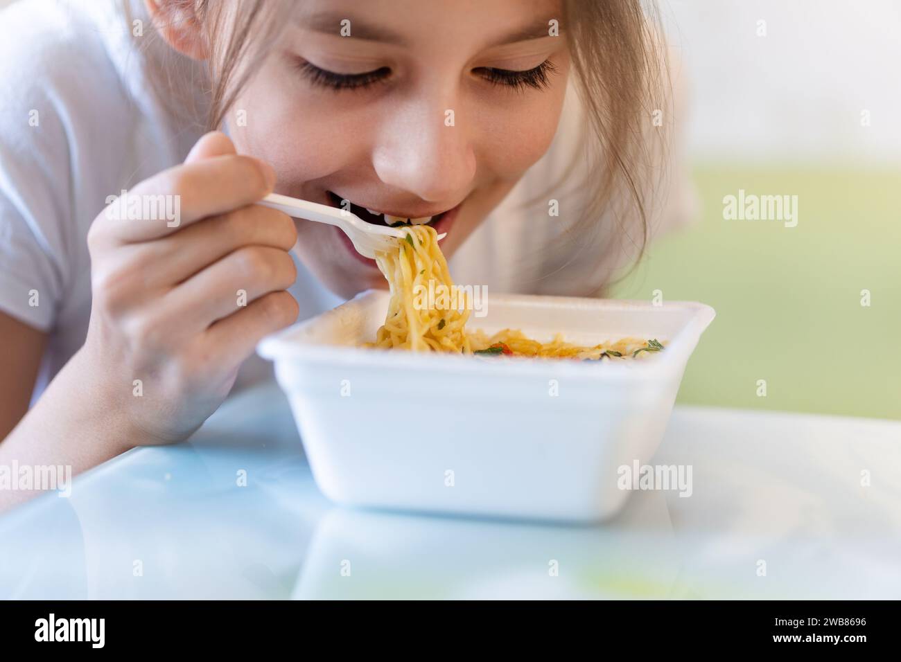 Ragazza che mangia spaghetti istantanei coreani piccanti utilizzando le forchette. fast food malsano. nutrizione degli scolari Foto Stock