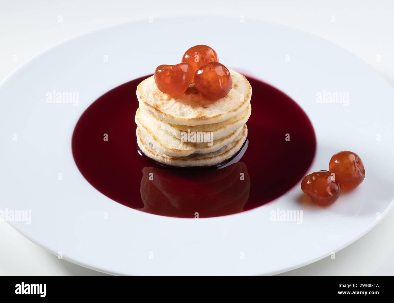 Una pila di pancake conditi con frutti di bosco rossi freschi disposti su un piatto bianco Foto Stock