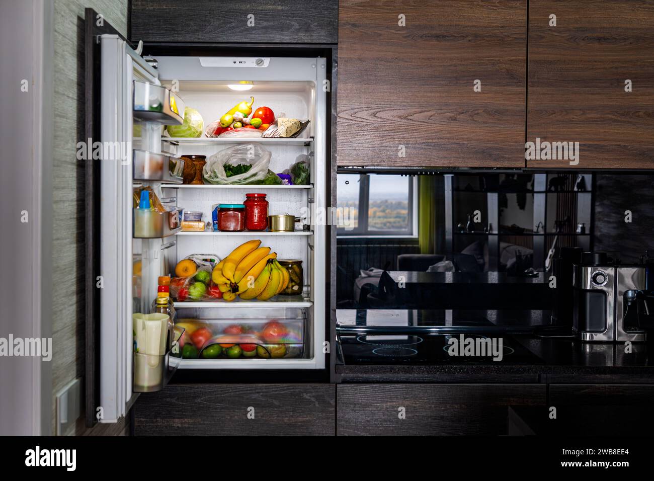 Grande frigorifero aperto con prodotti in cucina nera. Foto Stock