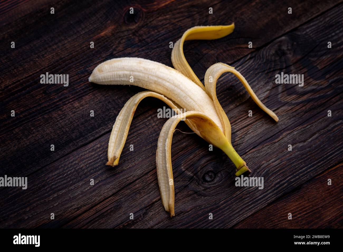Banana strammatura appena sbucciata con macchie, su un tavolo di legno Foto Stock
