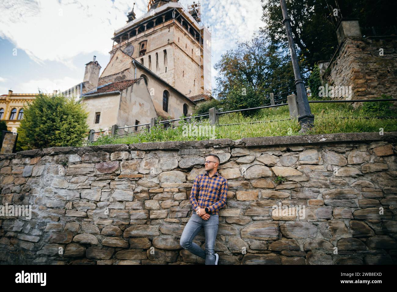 Giovane uomo d'affari in camicia appoggia la schiena contro le mura del castello nel centro storico di Sighisoara Foto Stock