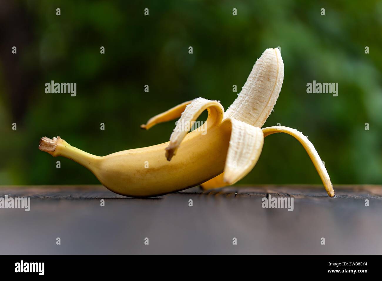 Composizione di frutta fresca, banana fresca e gustosa intera senza pelle su uno sfondo sfocato della natura Foto Stock