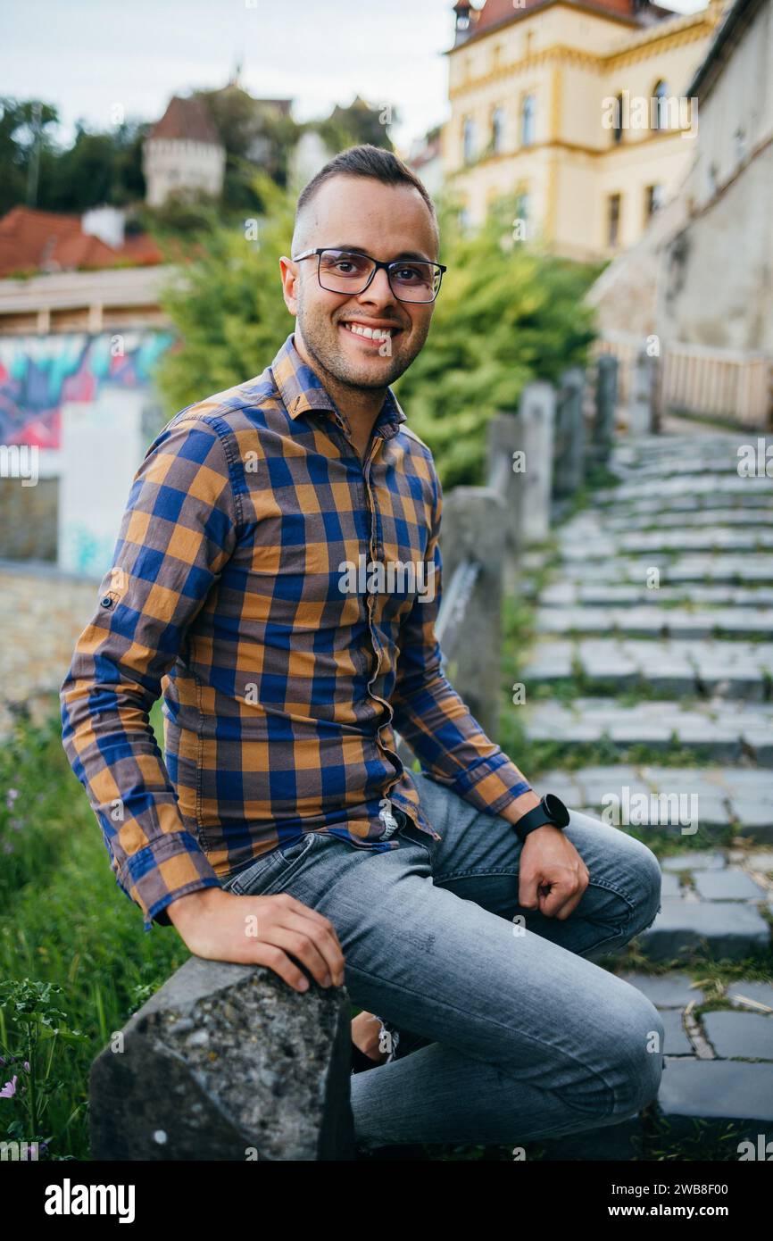 Un giovane con una camicia siede su una ringhiera e sorride Foto Stock