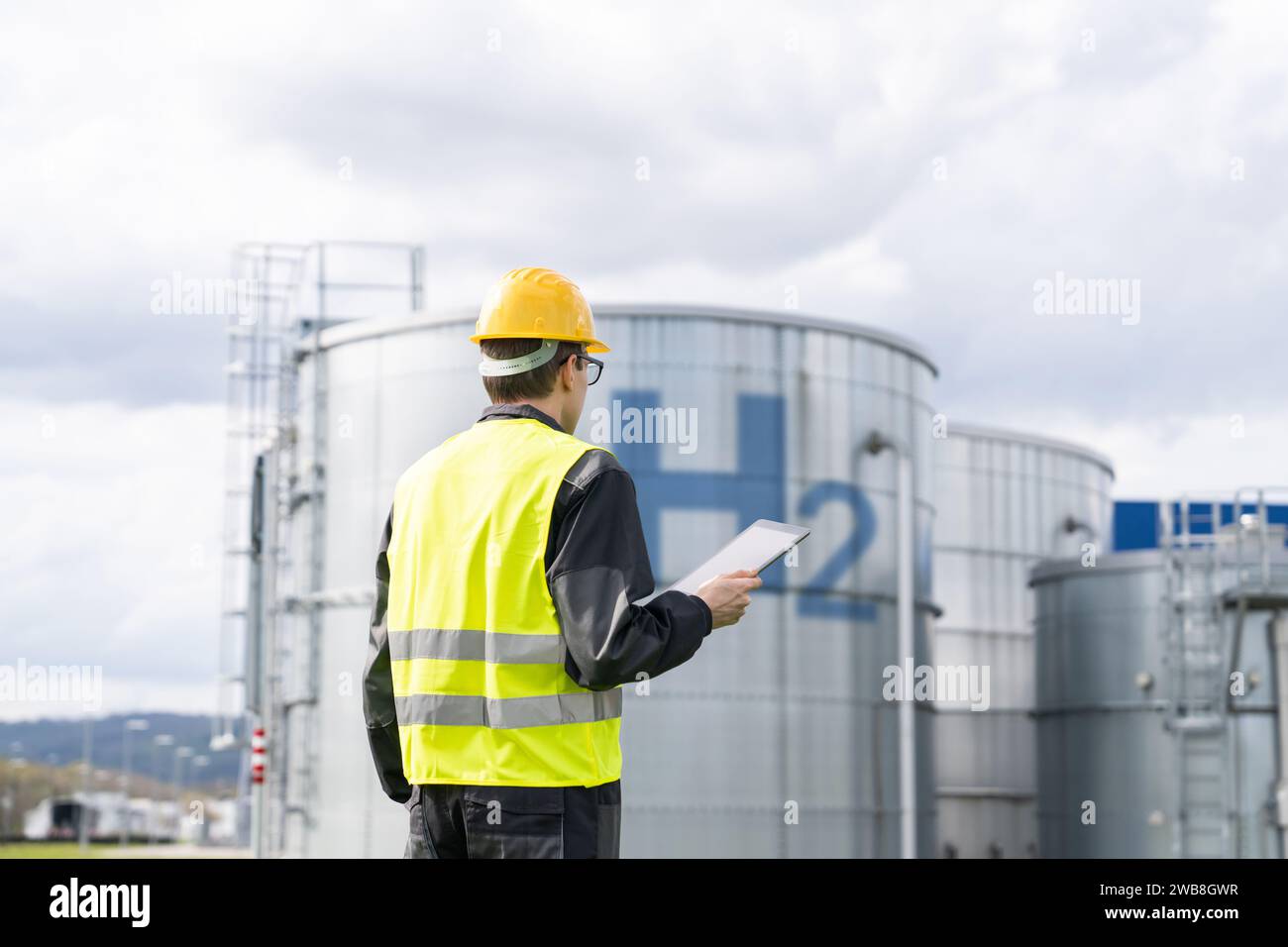 Ingegnere con computer tablet su uno sfondo di fabbrica di idrogeno. Foto Stock