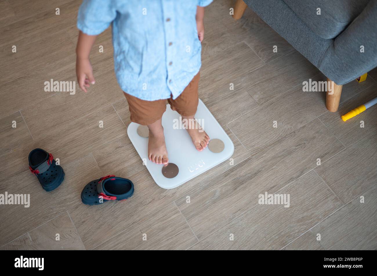 Bambino di due anni e mezzo, vestito con una camicia e bermuda, che fa un passo verso abitudini sane. In piedi scalzi su una smart scale i digitale Foto Stock