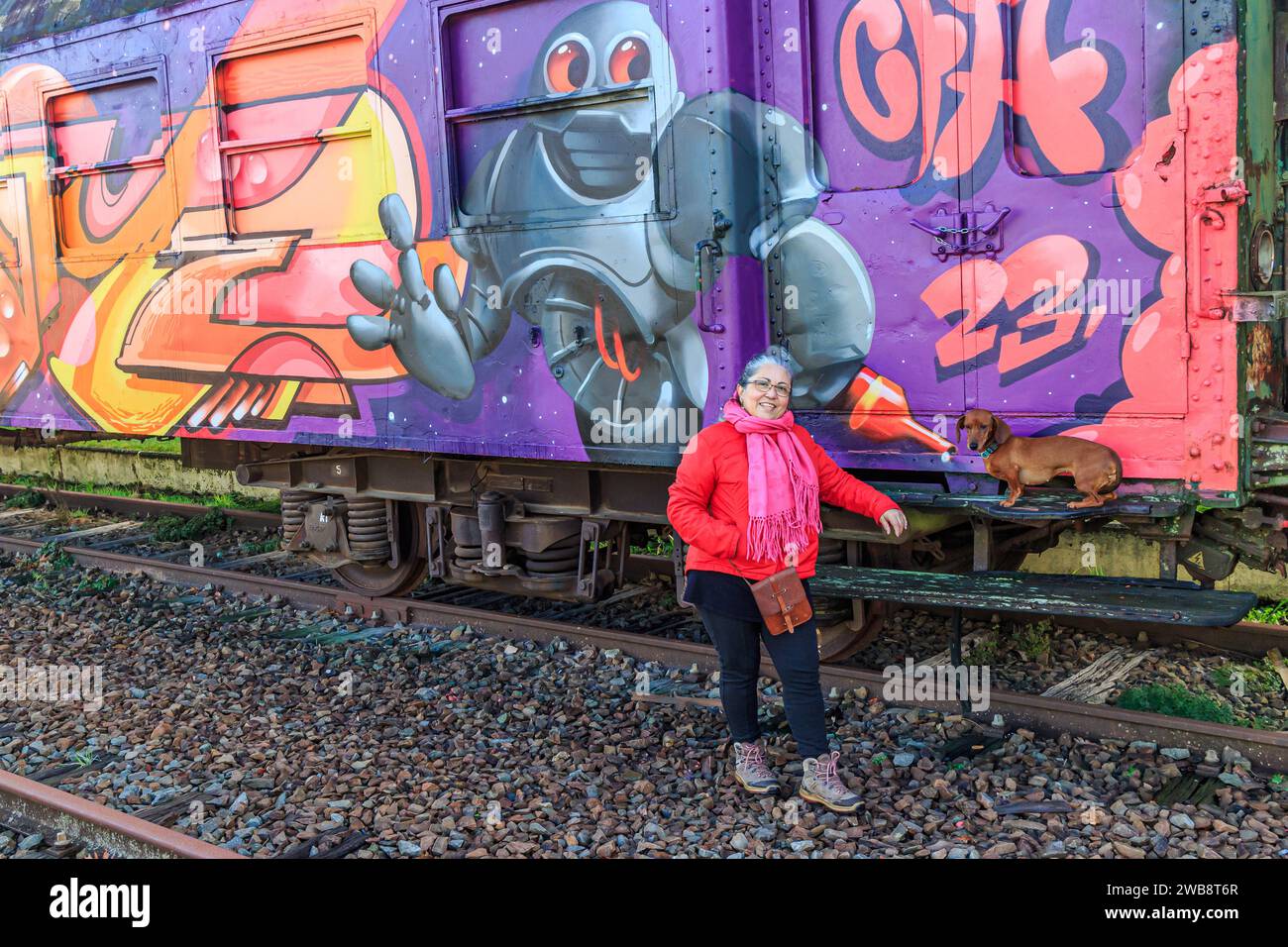 AS, Limburgo, Belgio. 17 dicembre 2023. Anziana turista in posa con il suo bassotto accanto all'autocarro dipinto con graffiti, tracce in disuso al Foto Stock