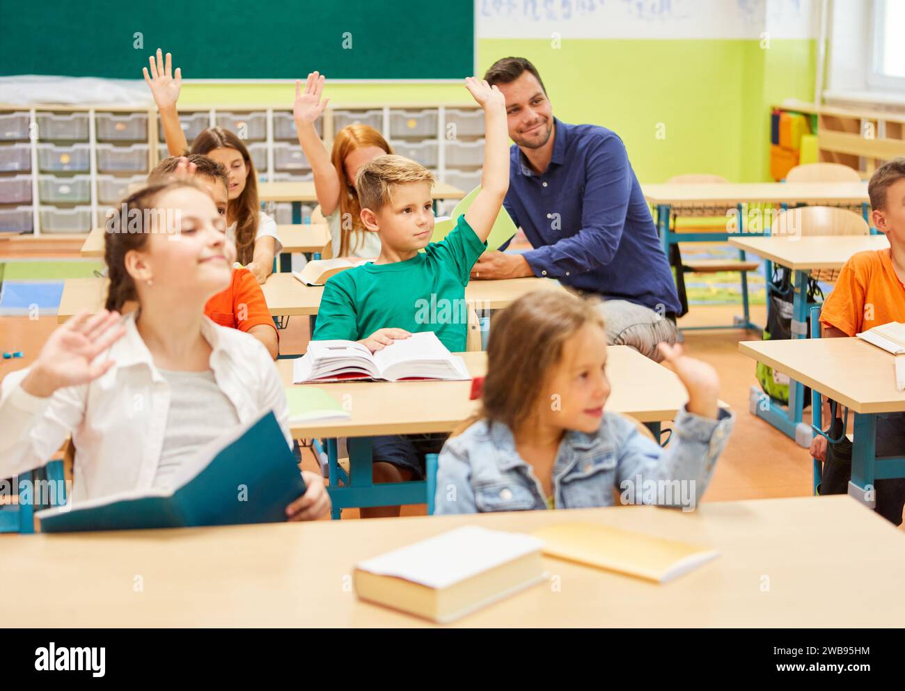 Studenti maschi e femmine che alzano la mano durante la lezione in classe a scuola Foto Stock