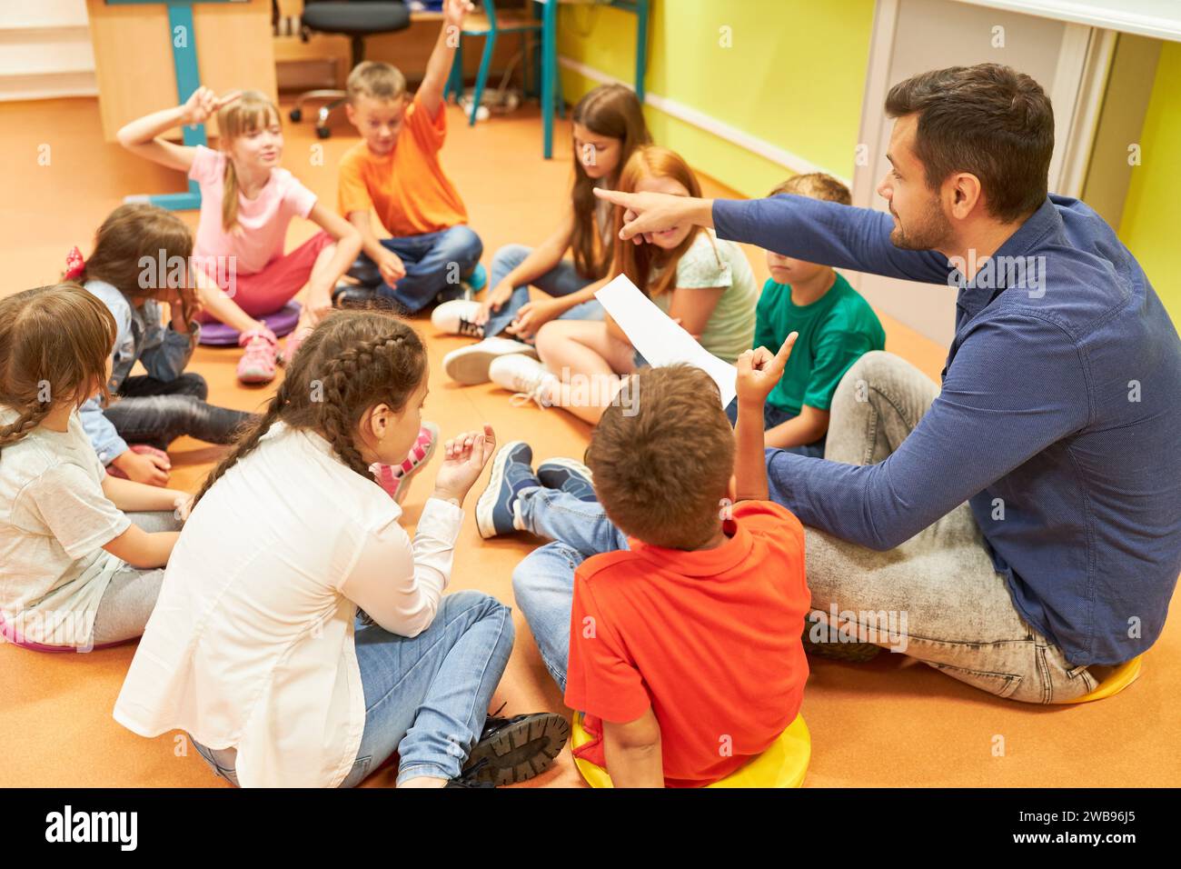 Insegnante elementare maschile che indica gli studenti seduti sul piano in classe Foto Stock