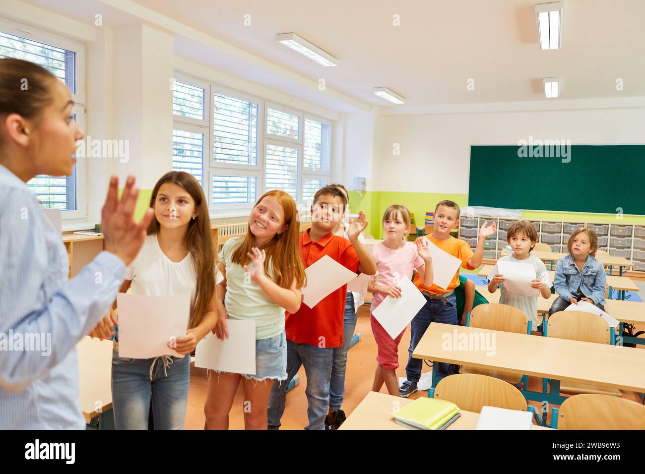 Gruppo di bambini delle scuole elementari che sventolano a insegnante femminile in classe Foto Stock