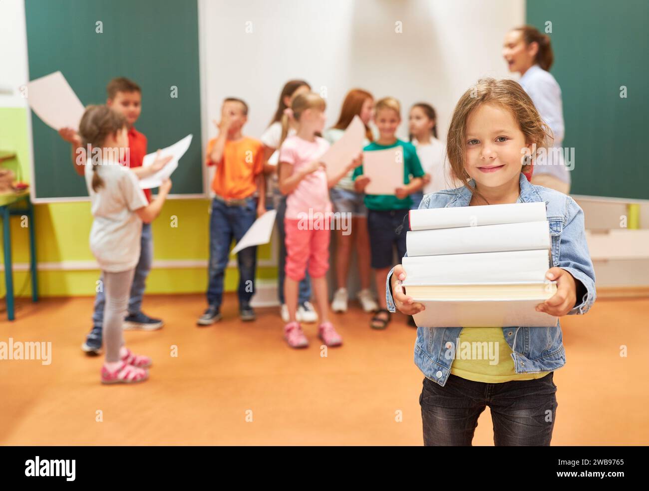 Ritratto di una studentessa elementare sorridente che tiene una pila di libri mentre si trova in classe Foto Stock