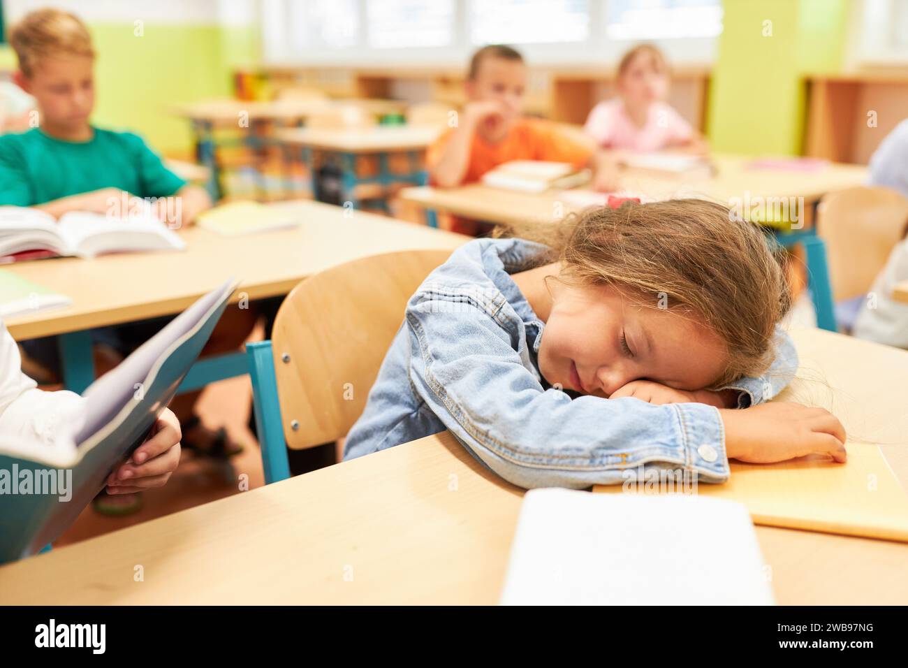 Studentessa elementare stanca che dorme sulla panchina in classe Foto Stock