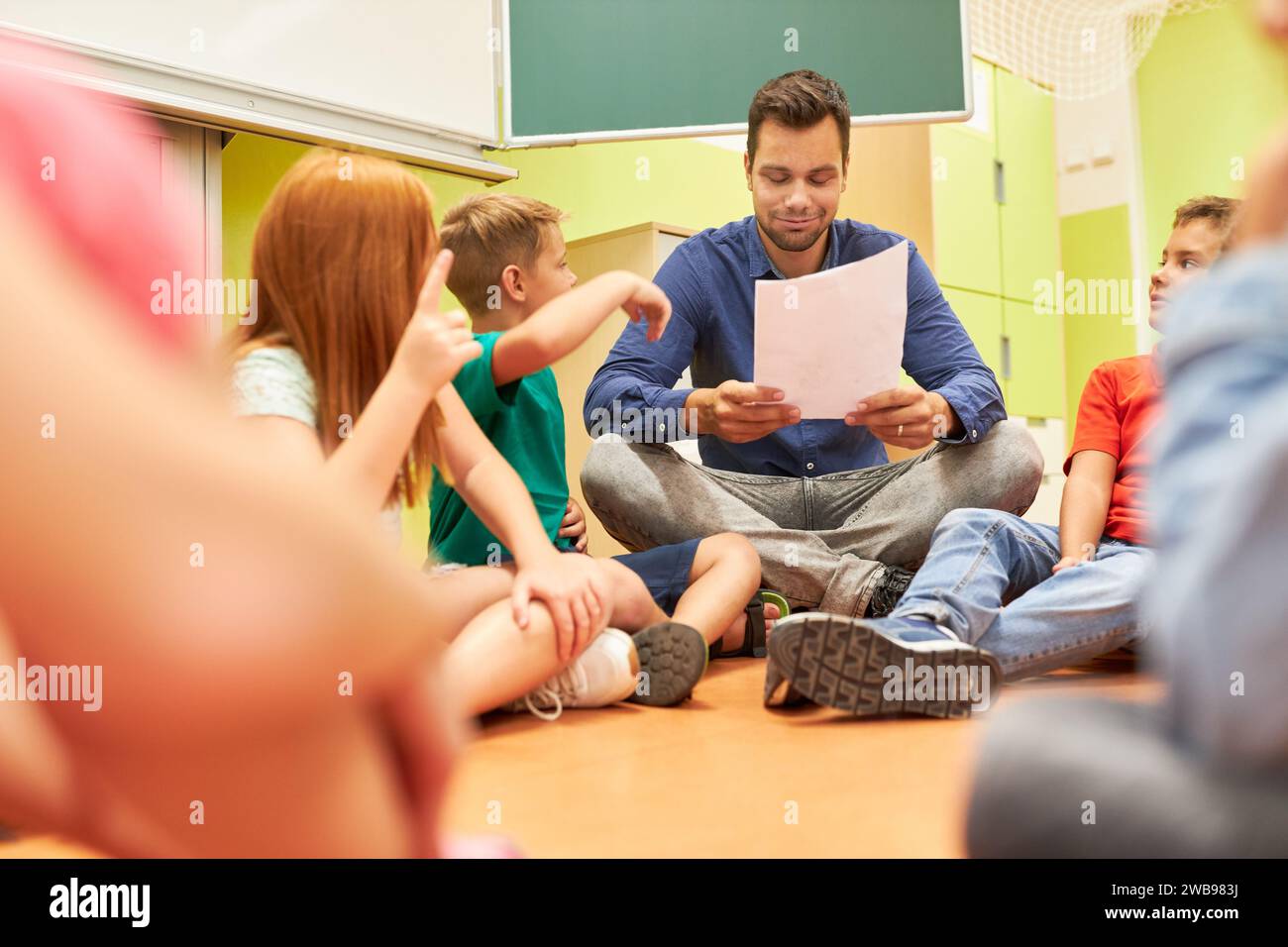 Insegnante di sesso maschile che tiene un foglio di carta e seduto al piano con gli studenti in classe Foto Stock