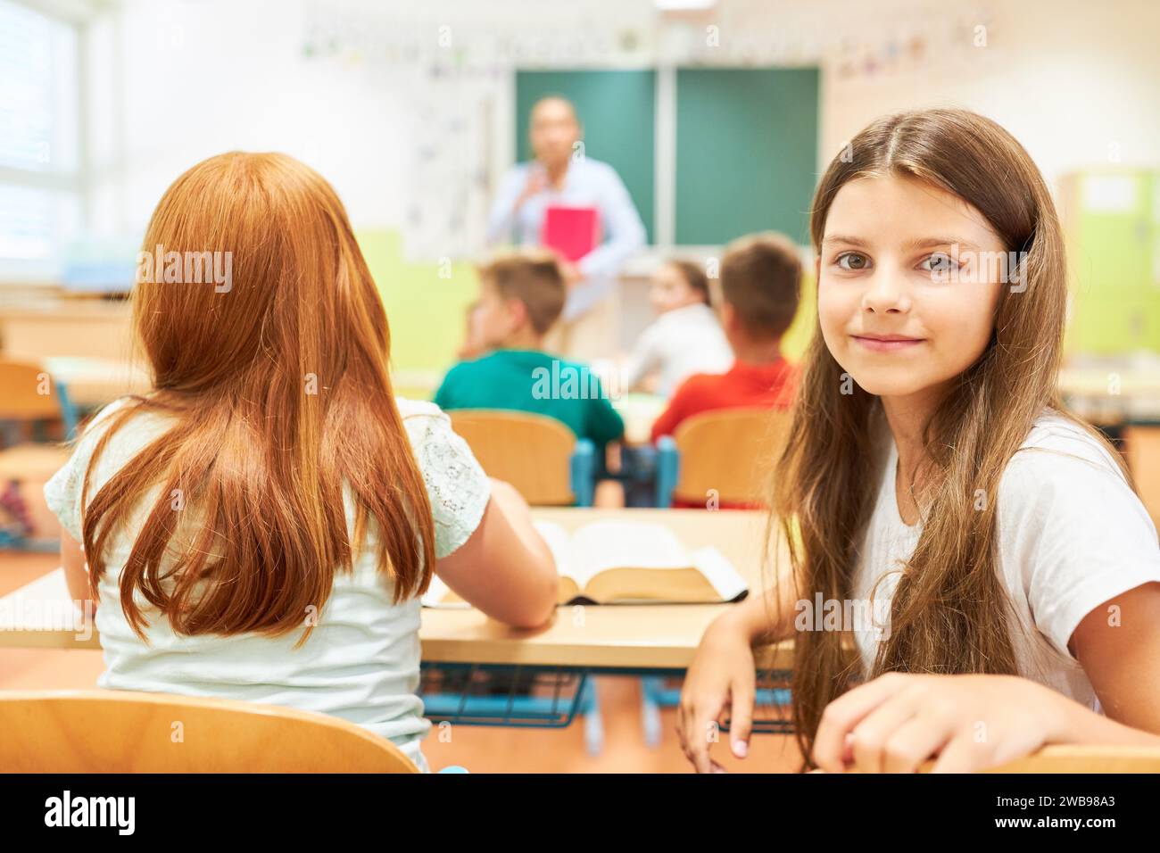 Ritratto di una studentessa elementare sorridente seduta con un'amica in classe Foto Stock