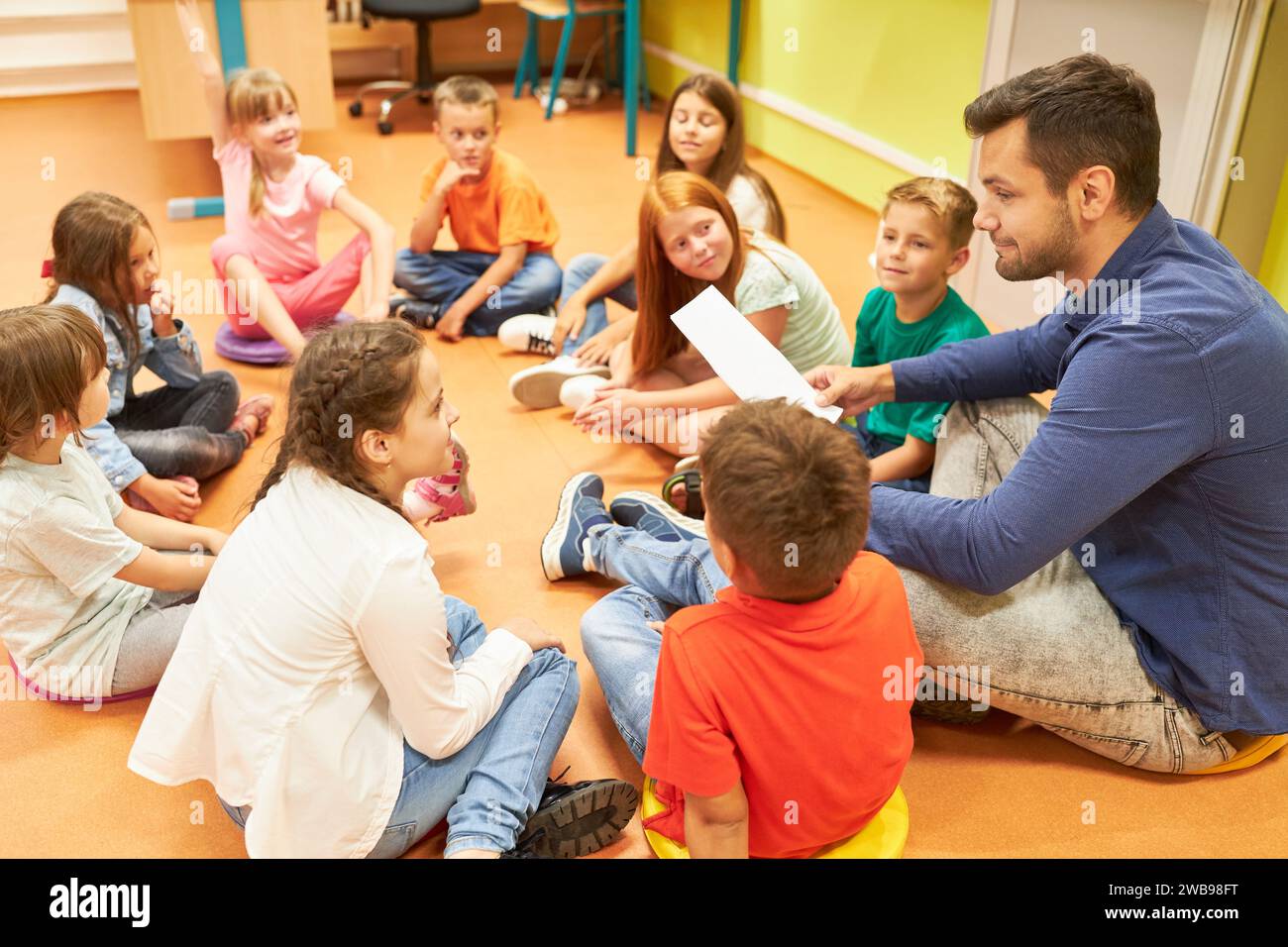 Insegnante di sesso maschile che tiene un foglio di carta mentre si siede con gli studenti sul piano in classe Foto Stock