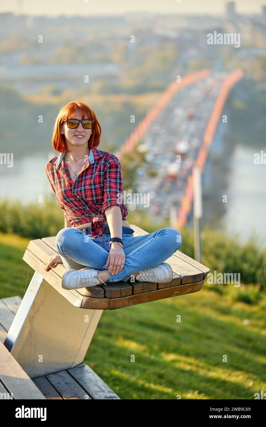 Una donna alla moda rossa che si gode una serata autunnale in città. Indossa una camicia rossa alla moda e jeans denim, per un'audace dichiarazione di stile Foto Stock