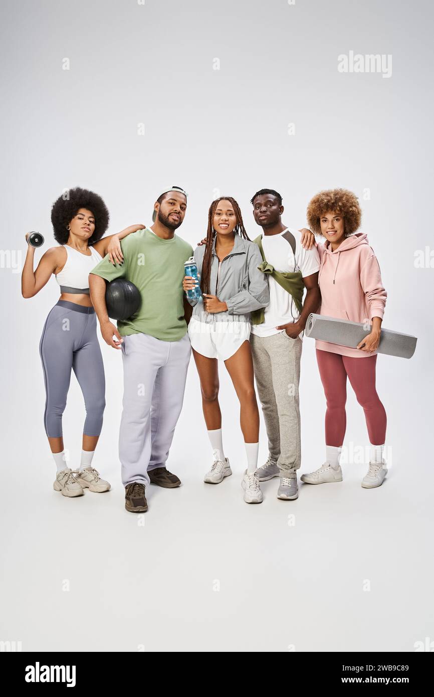 giovani amici afroamericani sportivi in piedi con attrezzature sportive su sfondo grigio Foto Stock