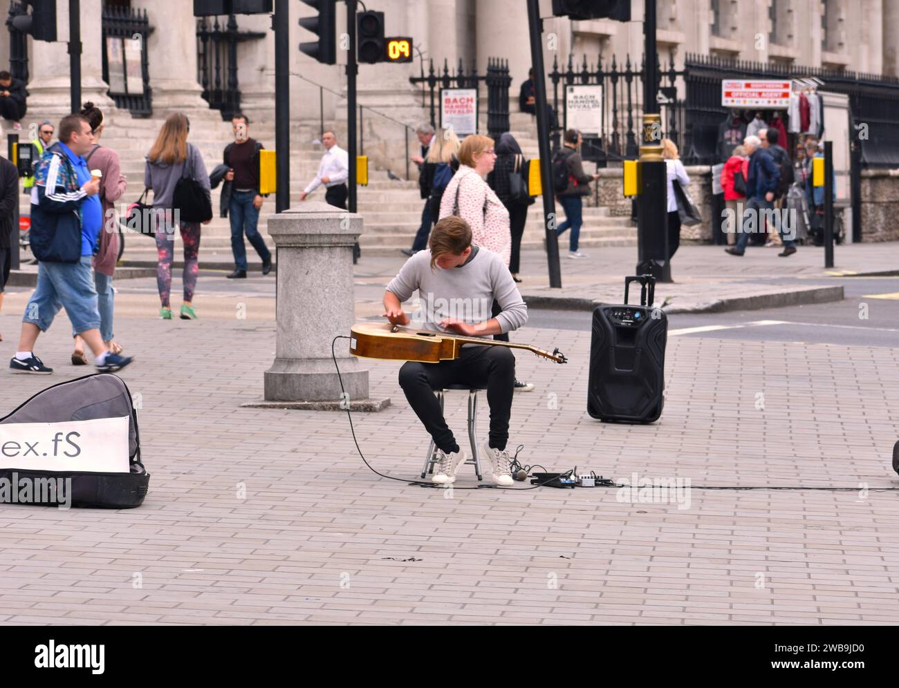 Un giovane maschio adulto che esegue un assolo di chitarra acustica su un marciapiede della città Foto Stock
