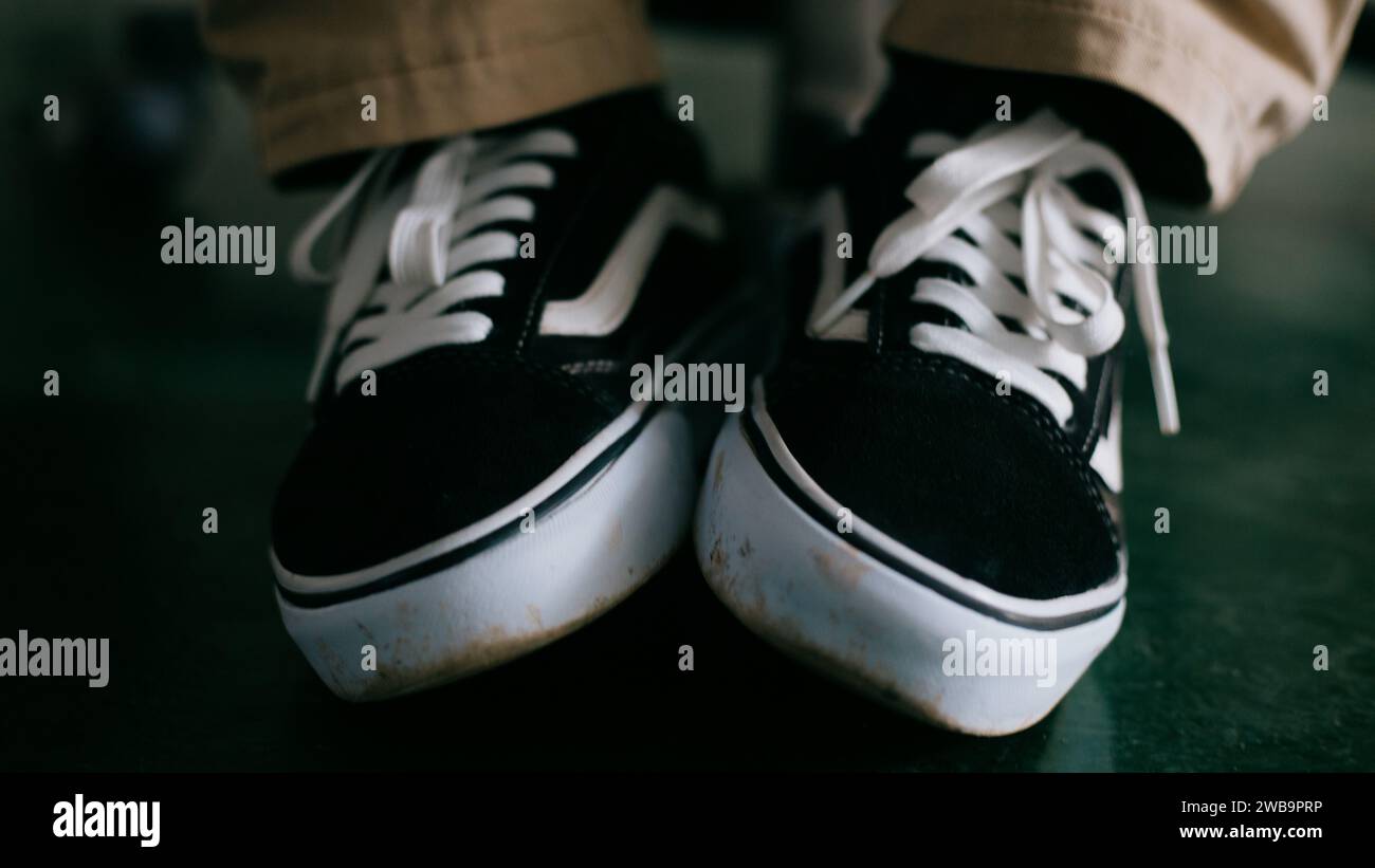 Un paio di sneaker bianche e nere con lacci bianchi, adagiate su uno sfondo marrone Foto Stock