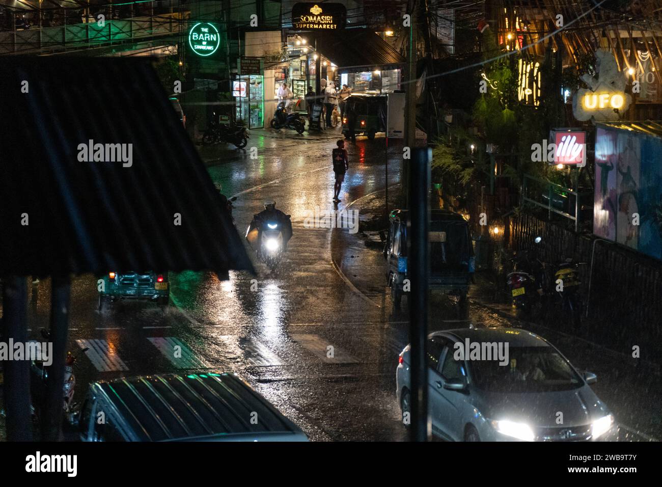 Ella, Sri Lanka, Asia - 18 dicembre 2023: Vista di una strada di Ella in Sri Lanka di notte e pioggia con tuk-tuk, auto e biciclette in movimento *** Blick auf eine Straße von ella in Sri Lanka bei Nacht und Regen mit fahrenden Tuk-tuks, Autos und Fahrrädern Foto Stock