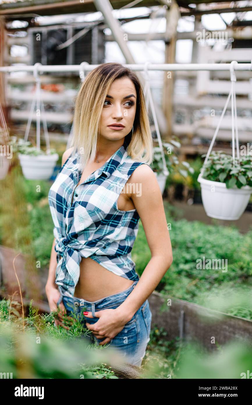 la ragazza in lungo cardigan nel negozio di piante sceglie tra due vasi di fiori rosa. Ritratto di gioiosa signora nel giardino botanico Foto Stock