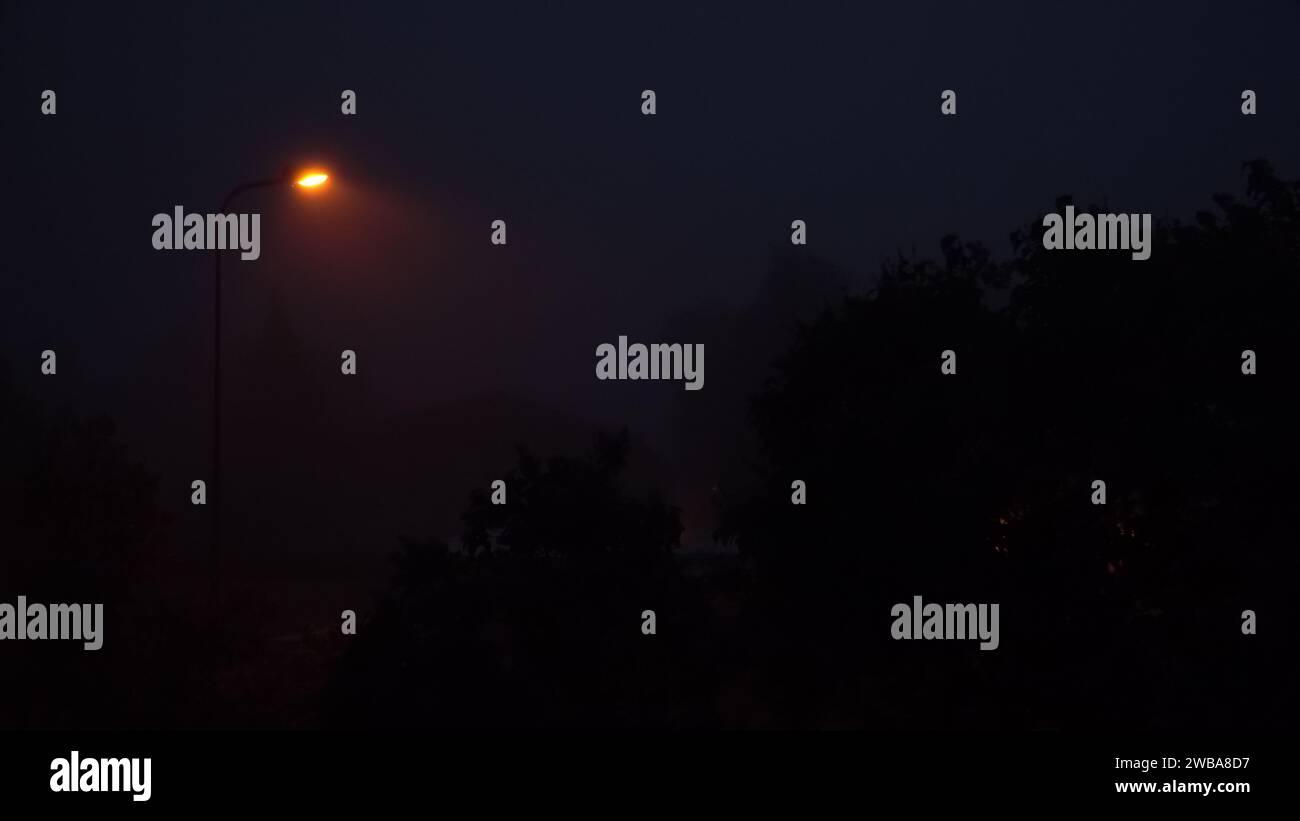 Nebbia in una città di notte. Una scena notturna spettrale con la luce gialla di una lanterna solitaria in una città nebbiosa, su uno sfondo blu scuro. Una sce Foto Stock