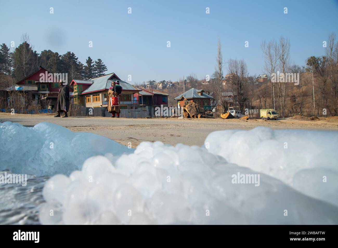 Un uomo e una donna Kashmiri aspettano un autobus che si forma a causa della fuoriuscita di acqua da un tubo nella periferia del villaggio di Srinagar. Il Kashmir si trova attualmente nel bel mezzo del rigido periodo invernale di 40 giorni, conosciuto localmente come "Chilla-i-Kalan". Durante questo periodo, un'onda di freddo estremo avvolge la regione himalayana, causando un calo delle temperature fino a -20 gradi. Ciò comporta il congelamento dei corpi idrici, tra cui il rinomato lago dal, e delle linee di approvvigionamento idrico in varie parti della valle. (Foto di Faisal Bashir/SOPA Images/Sipa USA) Foto Stock