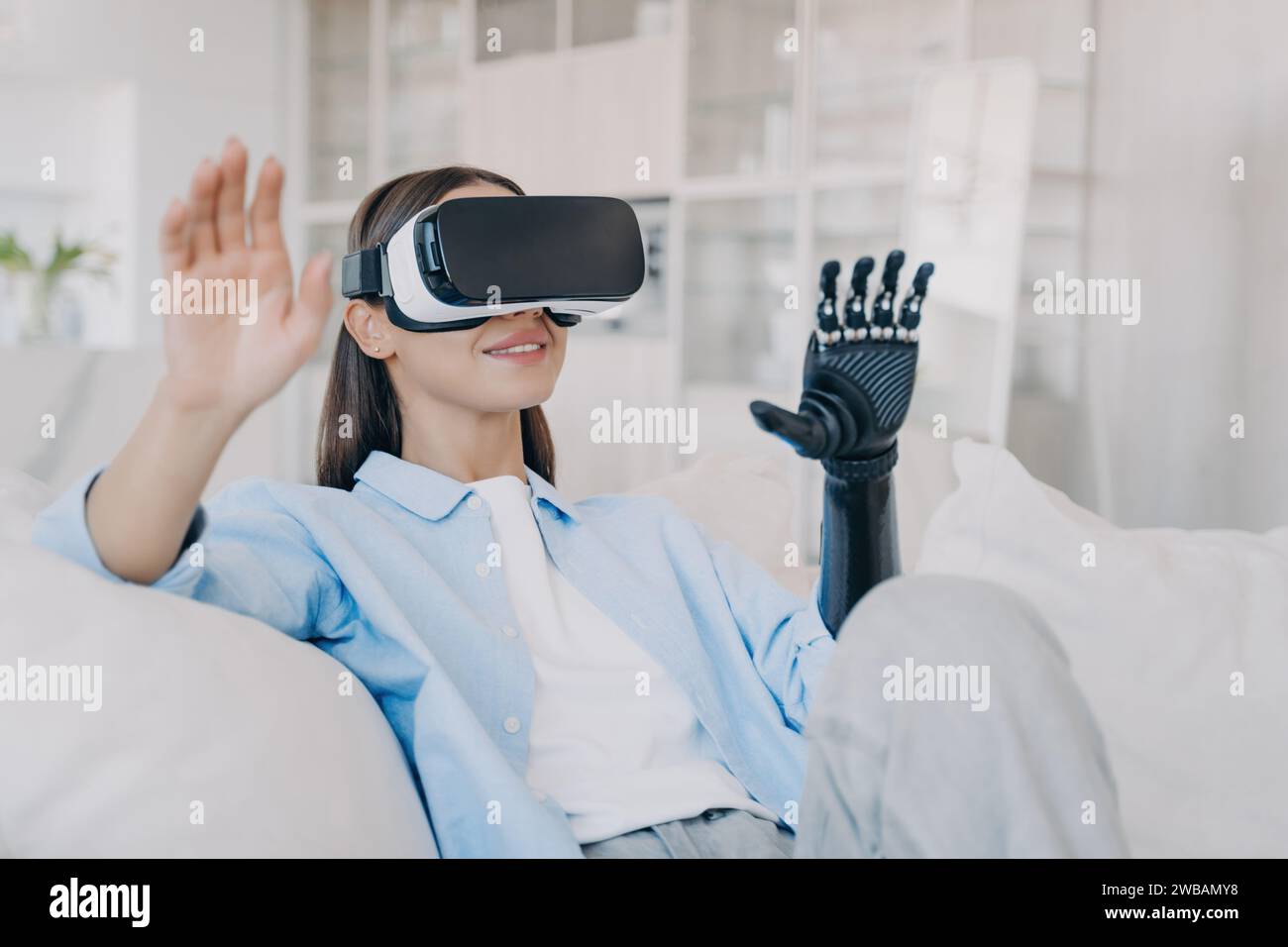 Una giovane donna con braccio bionico che esplora la realtà virtuale, seduta comodamente in un luminoso salotto Foto Stock