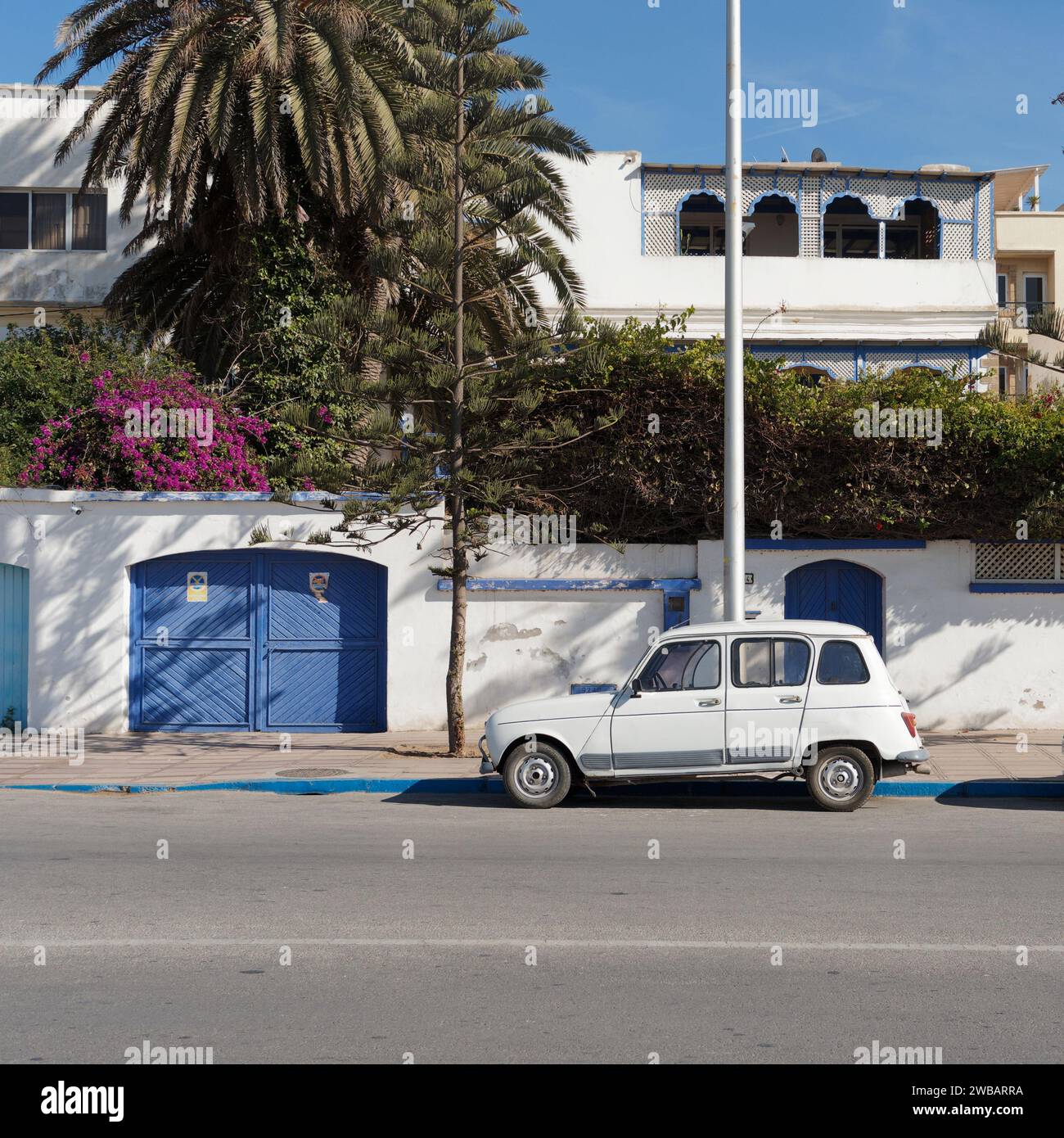 Vecchia auto bianca di fronte ad un albergo con cancelli d'ingresso blu nella città di Essaouira, in Marocco. 8 gennaio 2024 Foto Stock