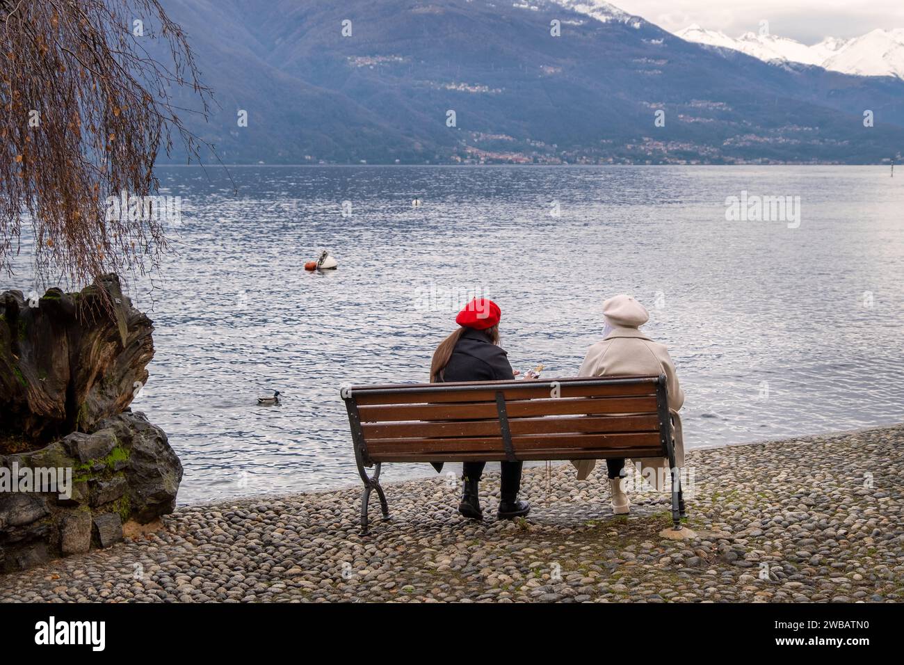 Giovani amici seduti su una panchina di legno di fronte al Lago di Como, Varenna, regione dei Laghi, Lombardia, Italia Foto Stock