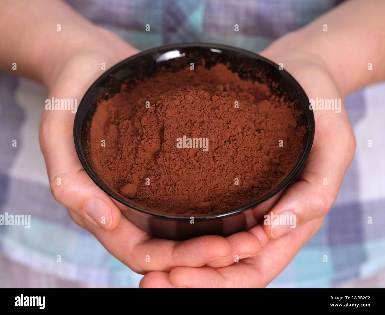 Una donna che tiene in mano una ciotola nera con polvere di cacao organico. Primo piano. Foto Stock