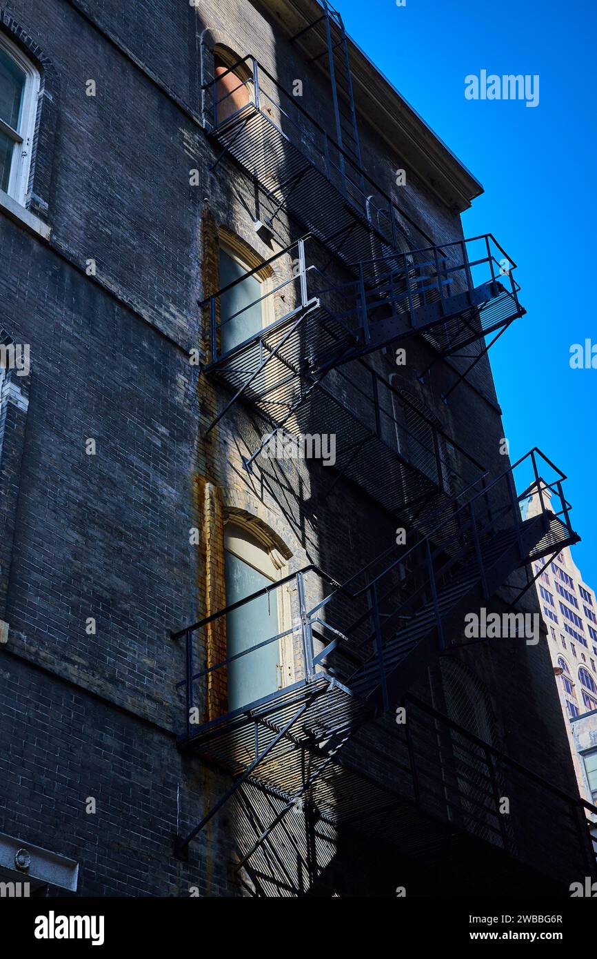 Urban Fire Escape Shadows sulla facciata in mattoni con sfondo Blue Sky Foto Stock