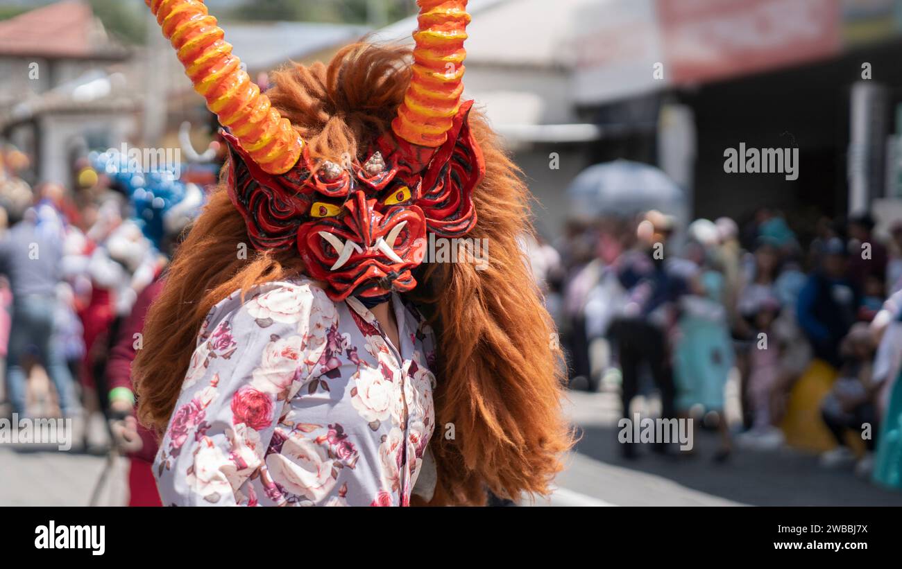 Pillaro, Tungurahua / Ecuador - 5 gennaio 2024: Uomo vestito come un diavolo rosso e bianco con capelli castani che danzano nella parata Diablada Pillarena nel c Foto Stock