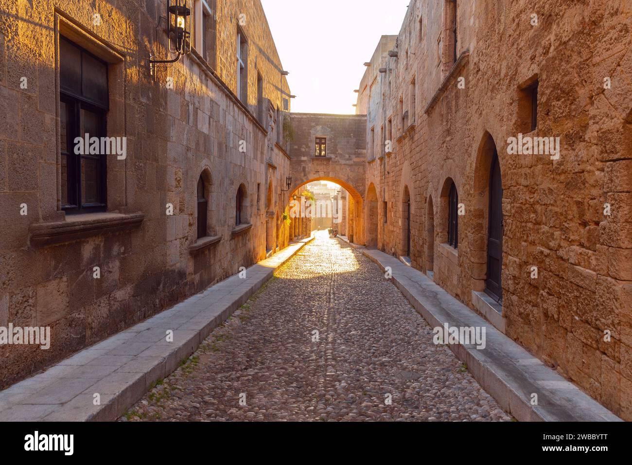 Una stretta strada medievale in pietra illuminata dal sole mattutino nella città vecchia. Rhodes. Grecia. Foto Stock