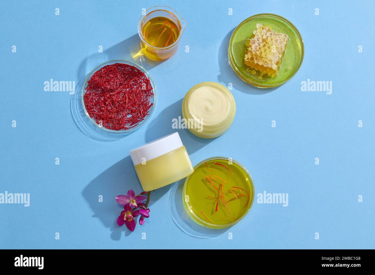 Sullo sfondo blu, vasetti gialli senza etichetta decorati con piatti di petri contenenti stigmi, zafferano, essenza gialla e cera d'api. Mockup per adve Foto Stock