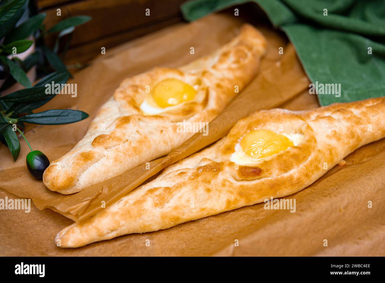 Khachapuri agiario della cucina georgiana, un pane a forma di barca ripieno di formaggio fuso e un uovo soleggiato, servito su carta pergamena. Foto Stock