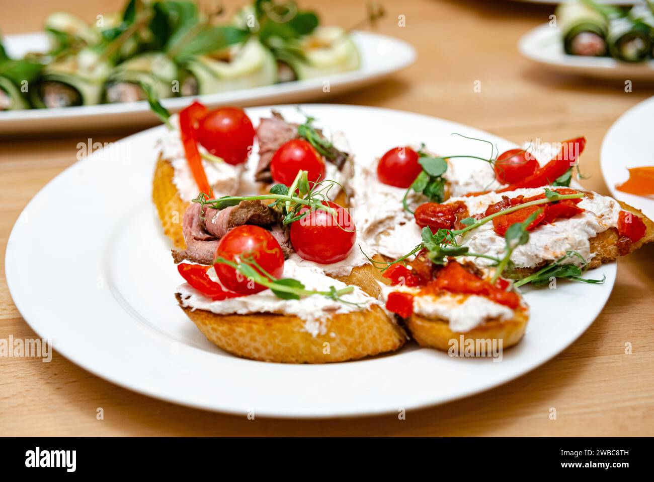 Deliziosa bruschetta condita con formaggio cremoso, succulente fette di manzo, pomodori ciliegini freschi e microgreen, disposta su un piatto bianco. Foto Stock