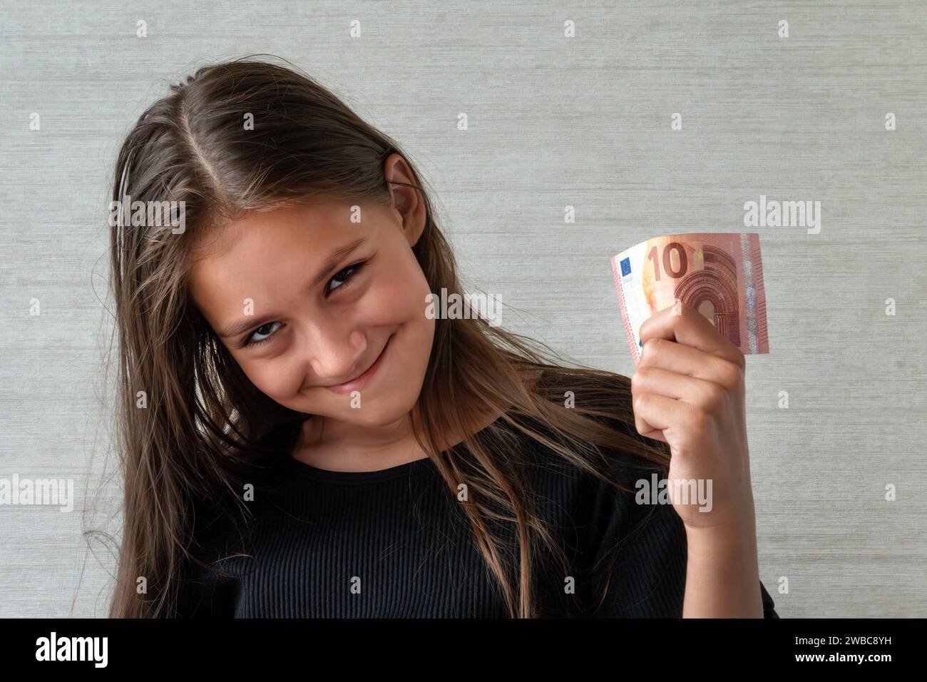 ragazza adolescente sorridente in pullover con dieci banconote da euro su sfondo grigio Foto Stock