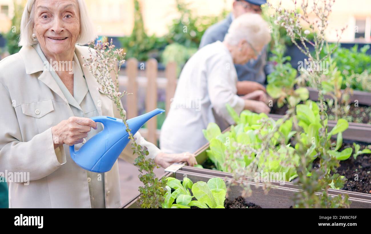 Vecchia sorridente mentre annaffiava un giardino in una geriatrica Foto Stock