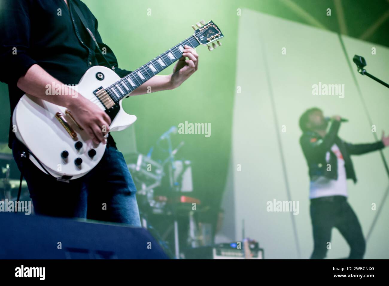 Un chitarrista rock è al centro del palco, le dita ballano sulla chitarra, mentre la band si sfuma dietro, aggiungendo una misteriosa atmosfera rock. Foto Stock