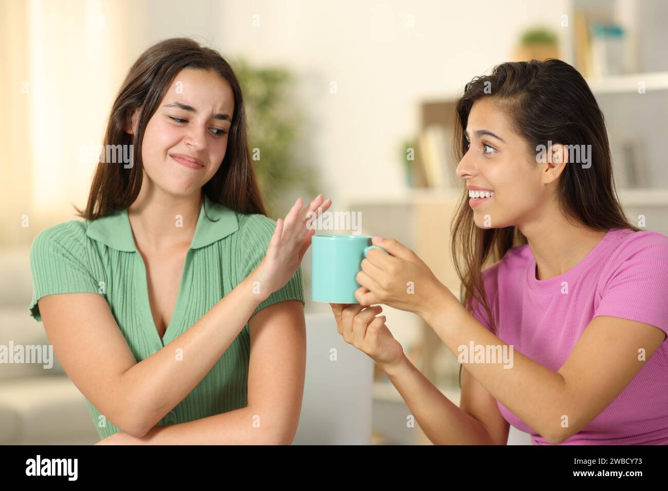 Donna che offre una tazza di caffè ad un amico che la rifiuta a casa Foto Stock