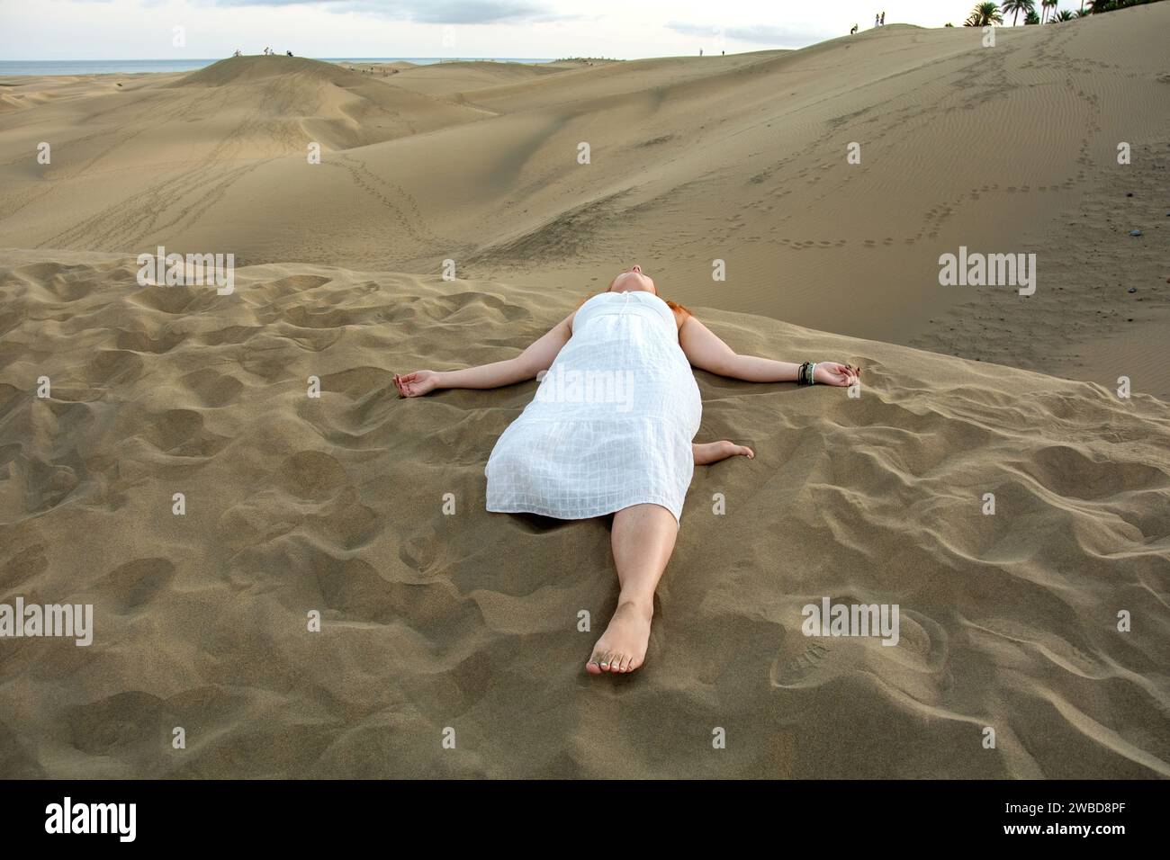 Una giovane ragazza giace tra le dune di sabbia con un vestito bianco Foto Stock