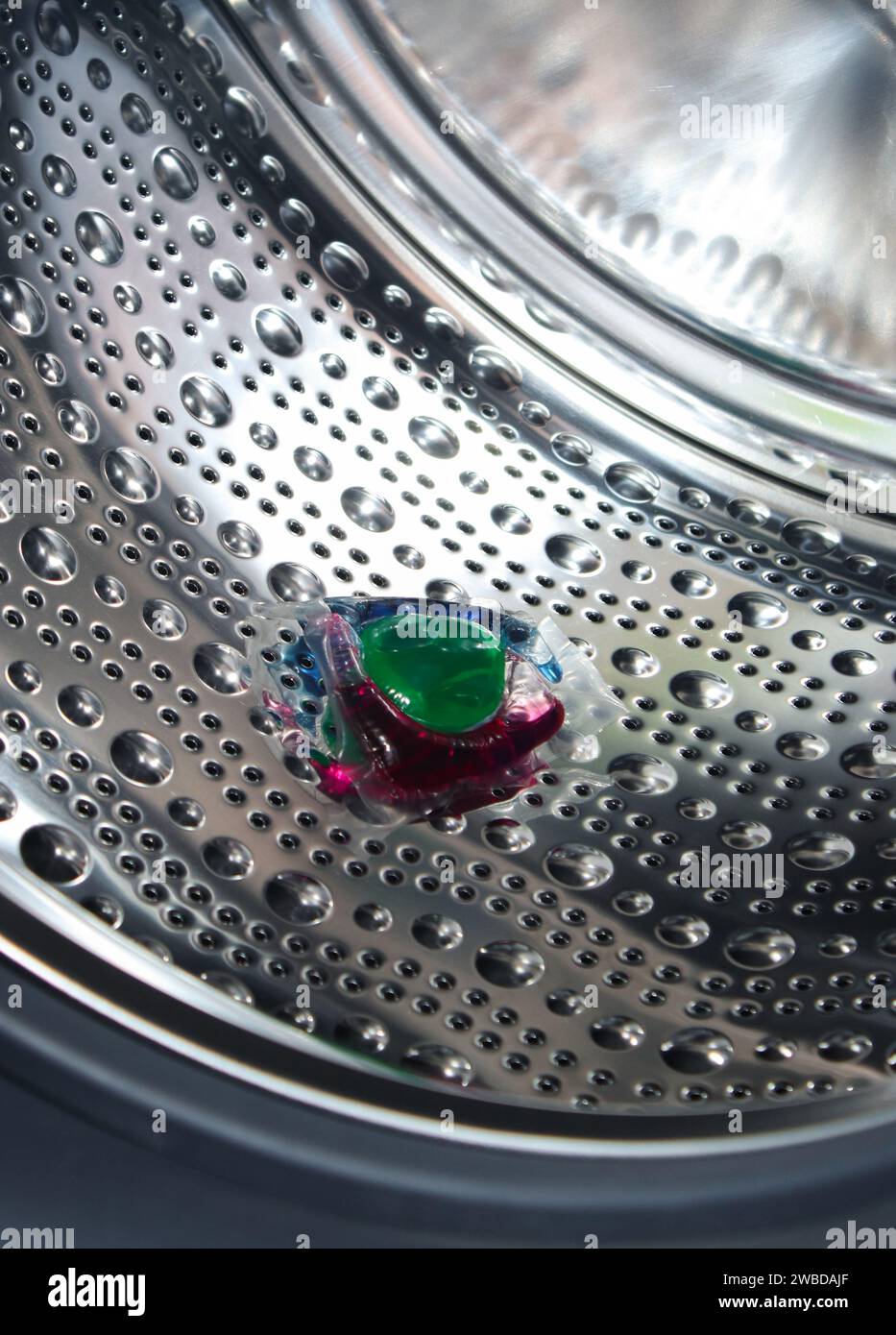 Gel detergente ecologico colorato in capsula in una lavatrice vuota Foto Stock