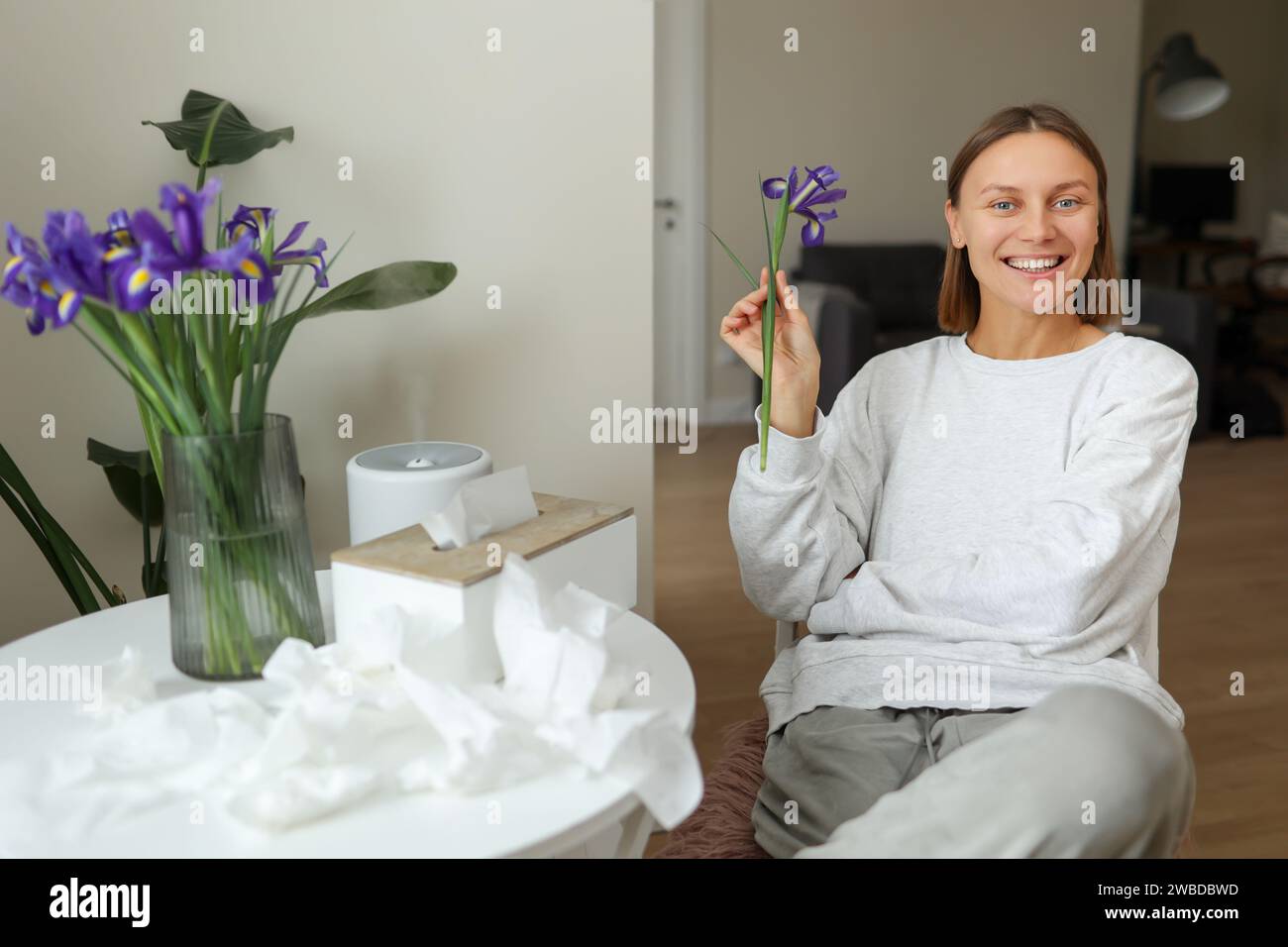 Senza allergie. Bella giovane donna tiene e annusa fiore d'iride, gode di odore senza sintomi naso che cola a casa. Bouquet di fiori primaverili al Foto Stock