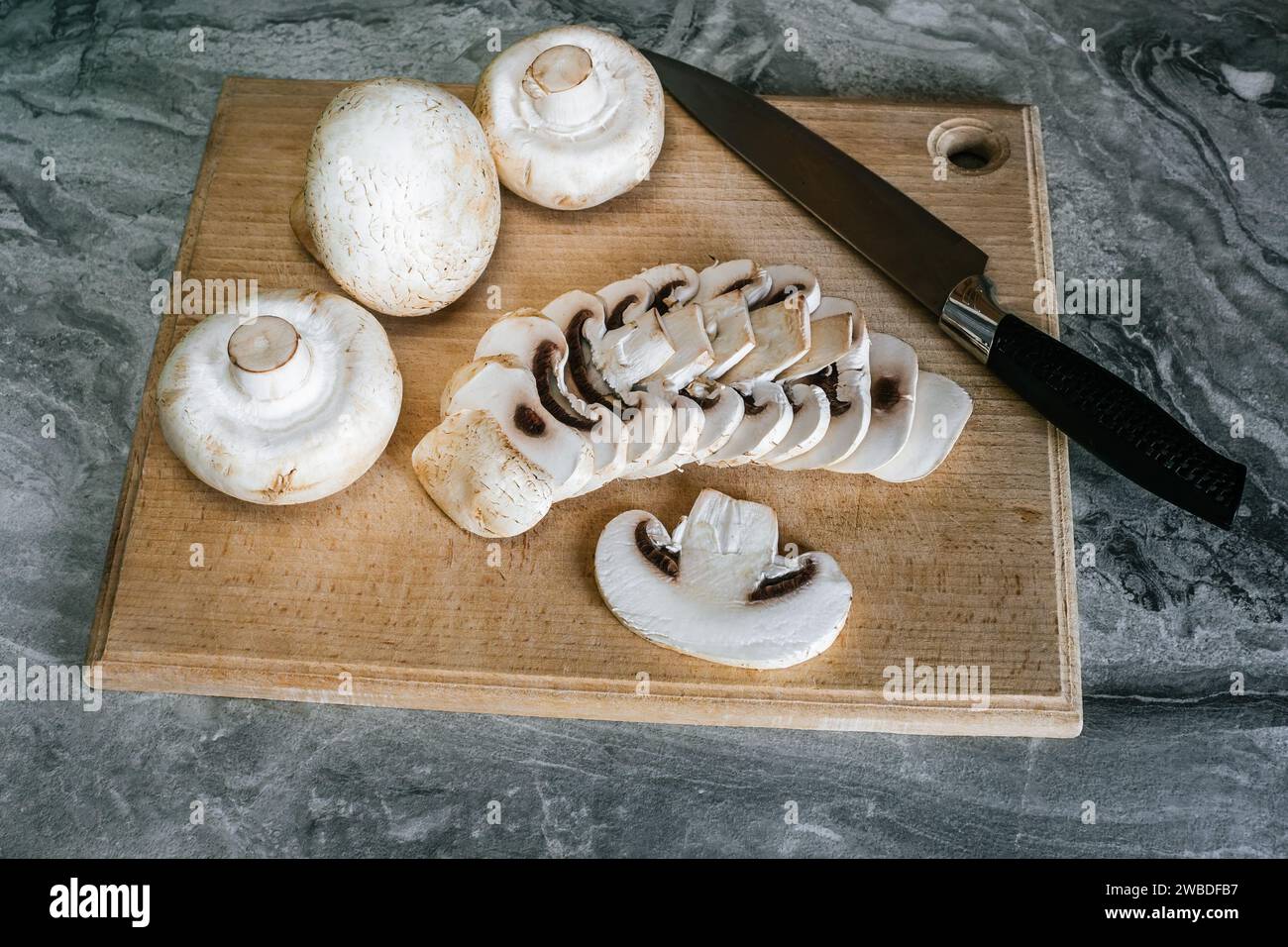 Vista dall'alto dei funghi champignon su un tagliere di faggio, uno dei quali è affettato ​​with un coltello Foto Stock