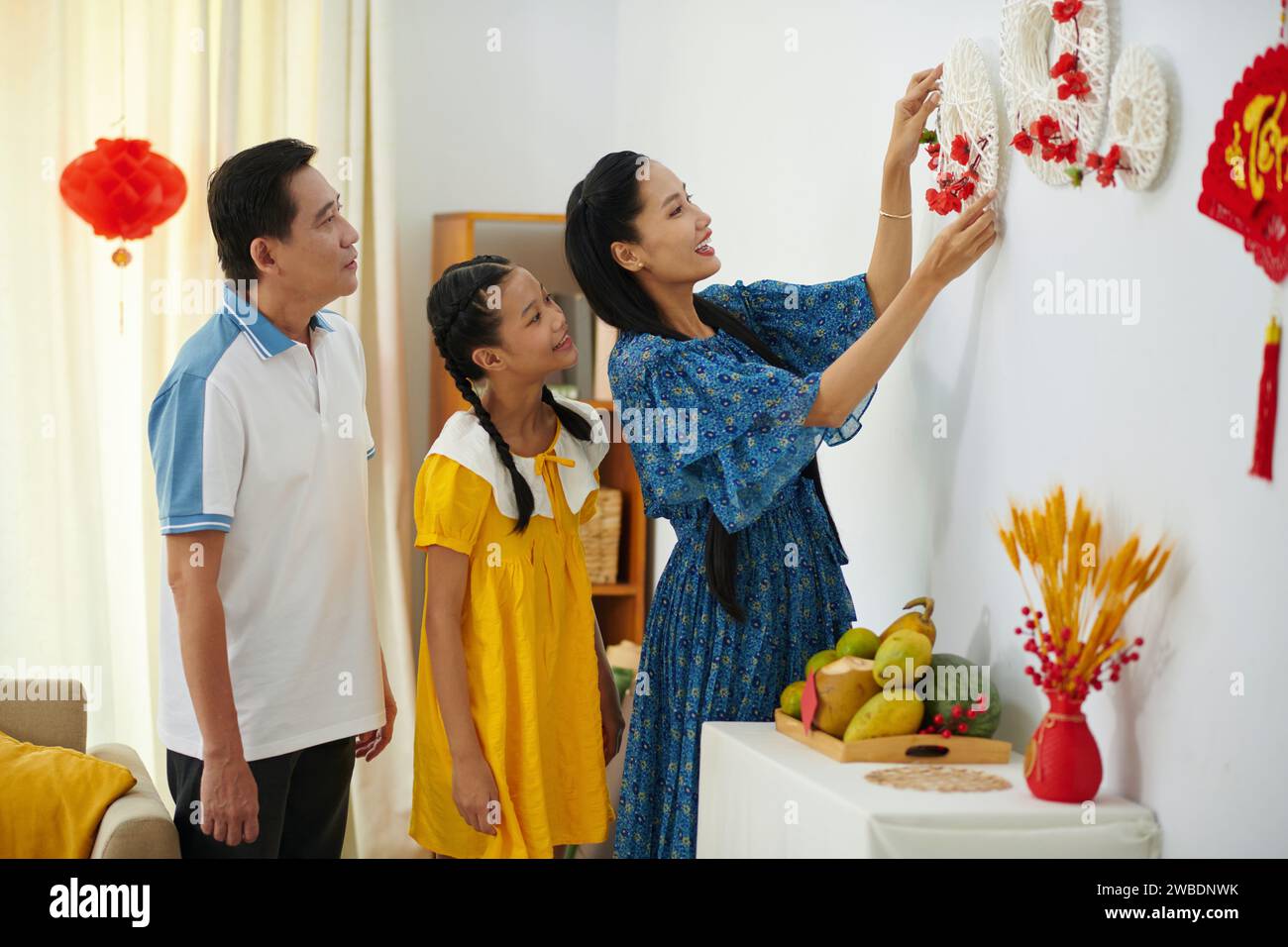 Allegra famiglia che appende le decorazioni Tet fatte a mano al muro Foto Stock
