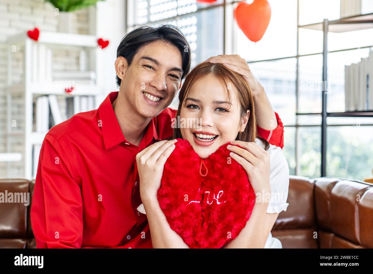 Una coppia felice che posa con i cuscini a forma di cuore nelle mani Foto Stock