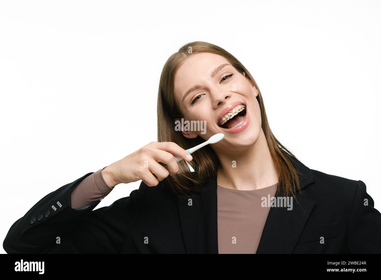 La ragazza sorride molto, tenendo in mano uno spazzolino da denti e mostrando bellissimi denti dritti con l'apparecchio. Foto Stock