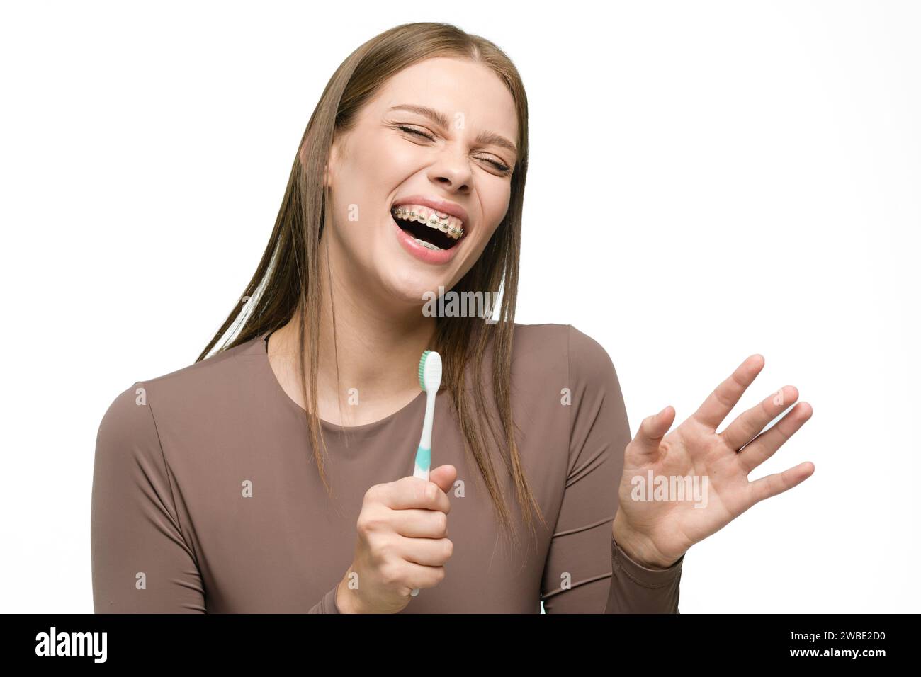 Giovane bella donna che canta allo spazzolino isolato su sfondo bianco. La ragazza sorride ampiamente mostrando bellissimi denti dritti con l'apparecchio. Foto Stock