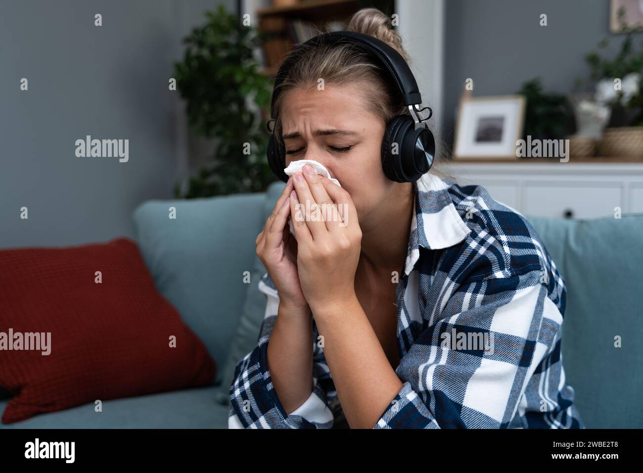 Giovane donna seduta a casa ad ascoltare audiolibri o podcast su cuffie wireless e a piangere. Si sente triste e depressa per il soggetto che hanno Foto Stock