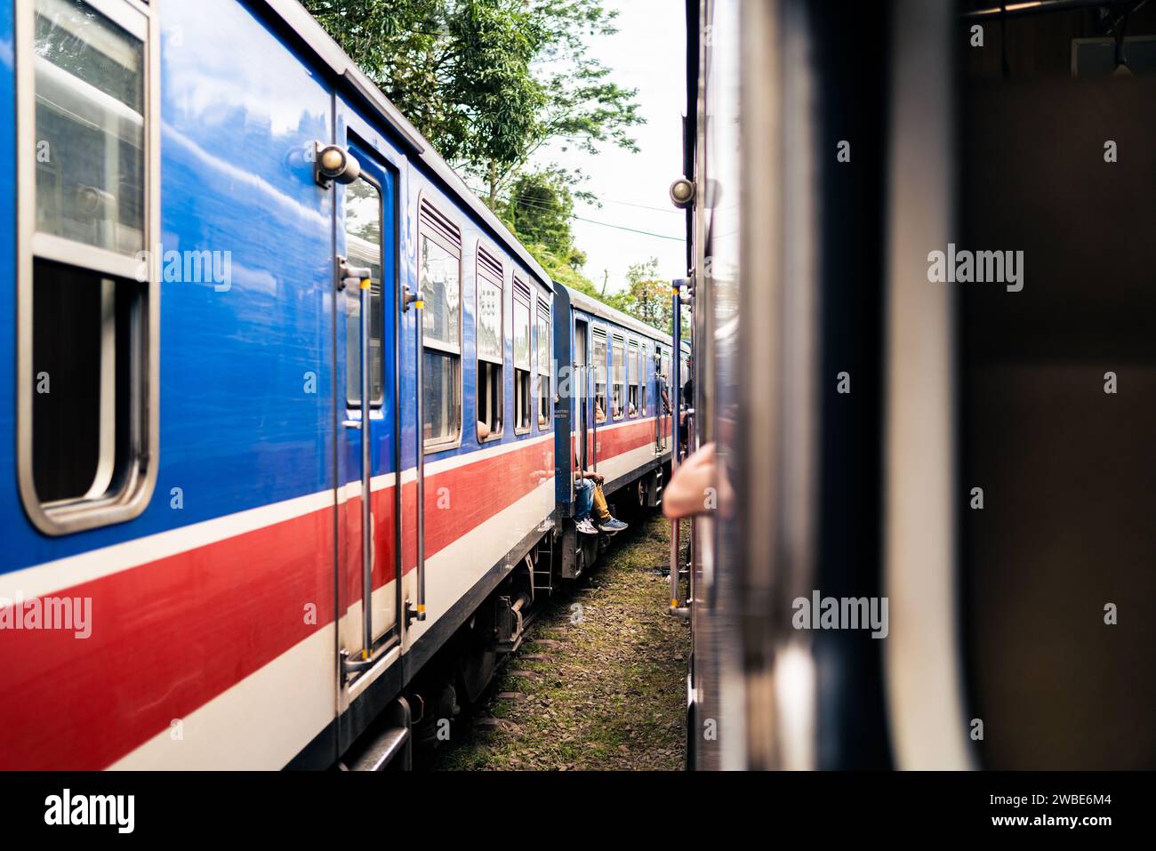 Due treni in Sri Lanka in attesa alla stazione. Viaggi ferroviari e turismo ferroviario. Vecchio pullman blu e rosso colorato. Ferrovia a Ceylon. Foto Stock
